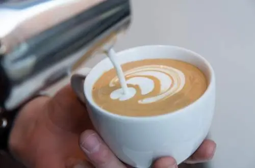 Pouring cream onto coffee to make latte art.